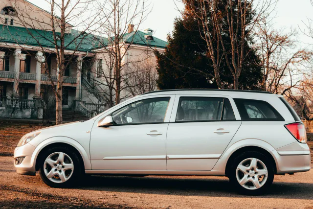 Srebrny Opel Astra kombi z boku przed domem