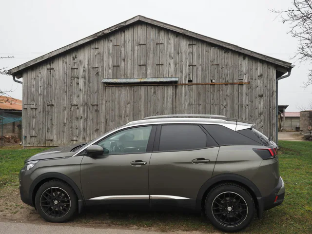 Szary Peugeot 3008 przed drewnianą stodołą, widok z boku